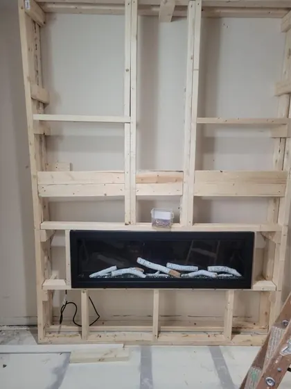 Wood framing built out from a living room wall for a linear electric fireplace and a wall-mounted TV