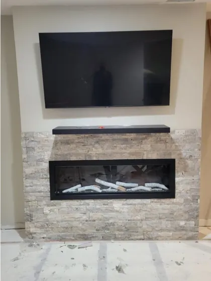 The finished wall with stacked stone veneer, a floating mantel, a soundbar and the TV mounted above the fireplace