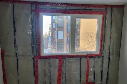 New insulation and a taped vapor barrier installed across the wall and around the window opening